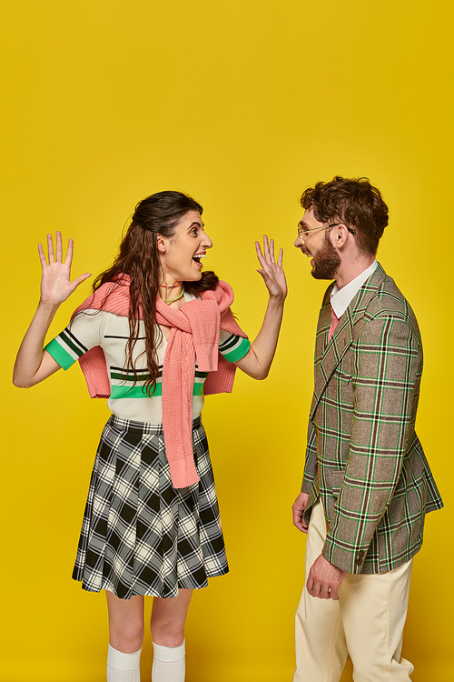 excited woman gesturing and looking at man on yellow backdrop, happy students, academic wear