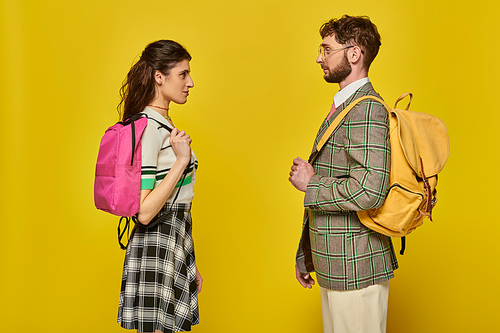 students standing with backpacks, face to face, looking at each other, yellow backdrop, college