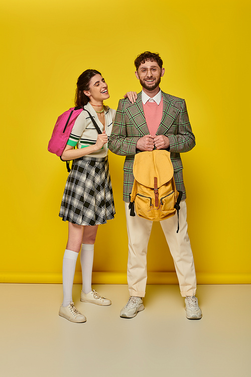students standing with backpacks, looking at camera, smiling, yellow backdrop, academic wear, style