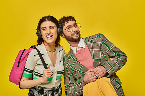 cheerful woman in wireless headphones standing near bearded man, students holding backpacks, music