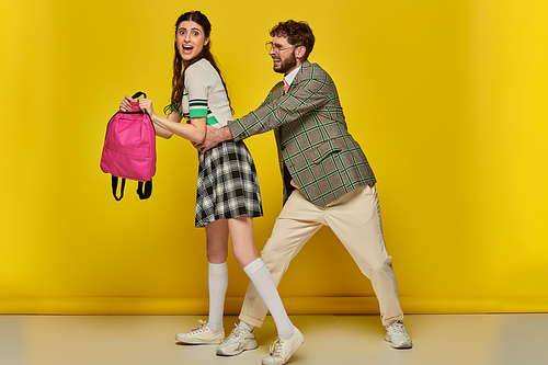 funny students, playful man hugging waist of female classmate on yellow backdrop, college life