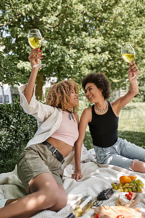 excited african american woman toasting with wine glass near girlfriend, enjoyment, picnic in park