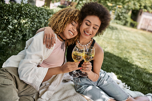 positive african american girlfriends with closed eyes clinking wine glasses, summer picnic in park