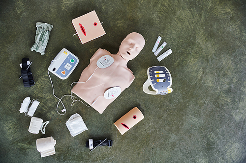 top view of CPR manikin, automated external defibrillator, wound care simulators, compressive tourniquets, bandages and syringes, medical equipment and first aid training concept