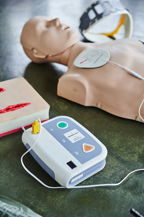 automated external defibrillator near wound care simulator, CPR manikin and neck brace on blurred background on floor in training room, medical equipment for first aid training