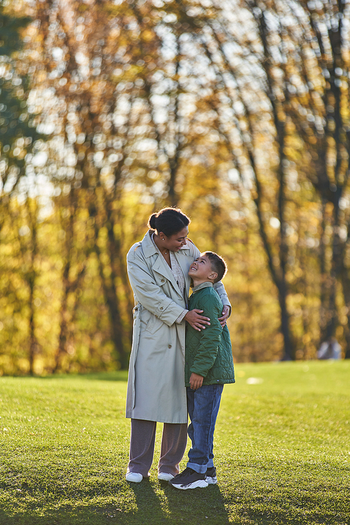 cheerful african american mother and son hugging in autumnal park, woman and boy in outerwear