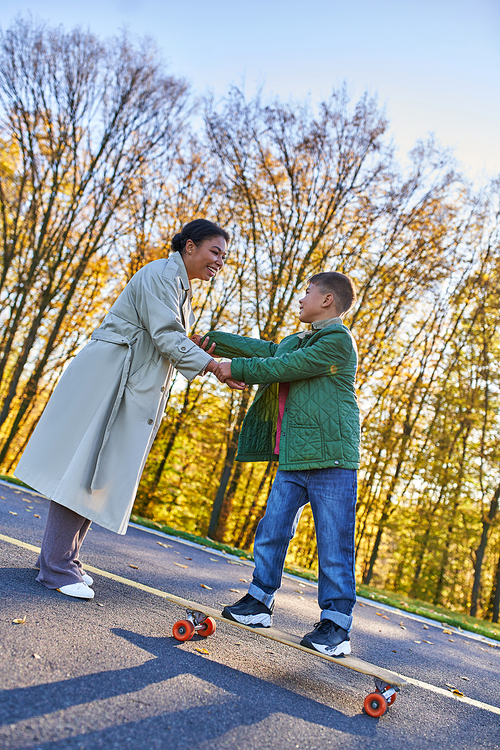 happy childhood, african american mother and son on penny board, woman and boy, hold hands, autumn