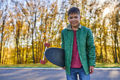 happy african american boy in outerwear holding penny board, autumn park, fall season, portrait