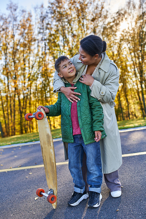 african american mother hugging son with penny board, autumn, fall season, motherly love, smile