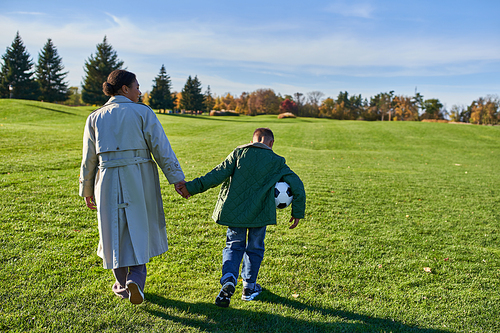 african american boy holding football, walking with mom on green field, holding hands, autumn