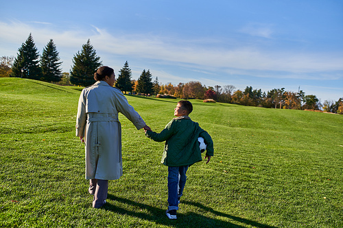 african american boy holding football, walking with mom on green field, holding hands, fall season