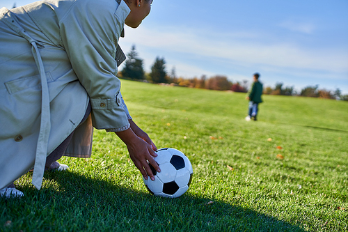african american woman with soccer ball, mother looking at son, blurred background, green field