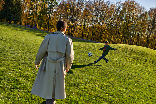 cute african american boy playing football near mother on green field, soccer, autumn, fall season