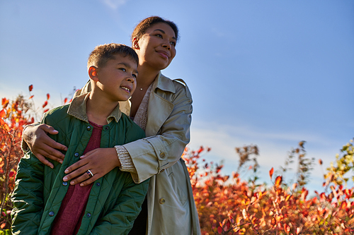 happy african american mother in autumnal clothes embracing son, fall season, golden leaves