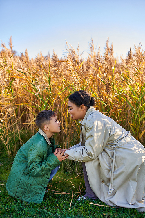 motherly love, african american mother in autumnal clothes holding hands of son, fall season