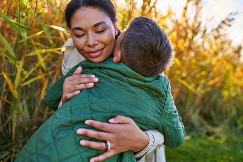 happiness, motherly love, african american mother hugging son in autumnal outerwear, fall season
