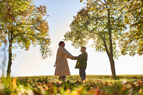 silhouette of mother and child holding hands in autumn park, fall season, bonding and love