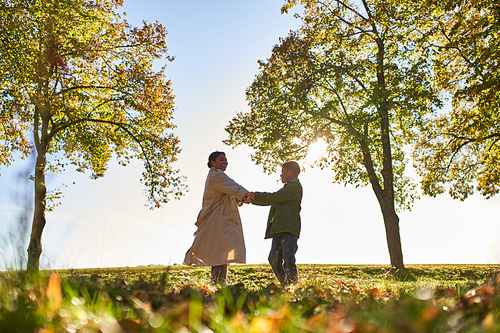 silhouette of woman and boy holding hands in autumn park, fall, bonding between mother and son