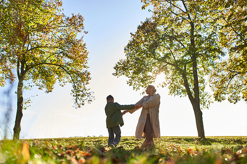 silhouette of mother and child holding hands in autumn park, fall season, having fun, freedom, dance