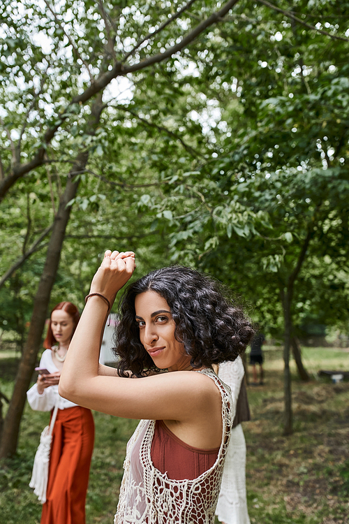 smiling multiracial woman in boho outfit looking at camera on lawn in retreat center