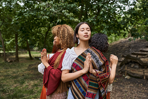 young interracial women doing praying hands gesture while standing in outdoor retreat center