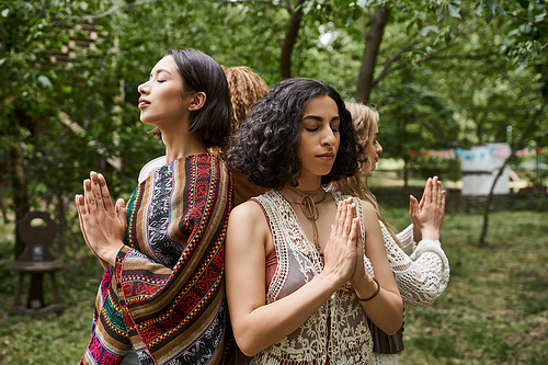multiracial woman with closed eyes doing praying hands gesture near friends in retreat center