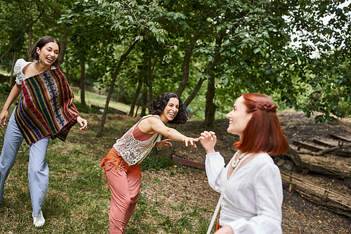 cheerful multiethnic women in boho outfits having fun on meadow in retreat center