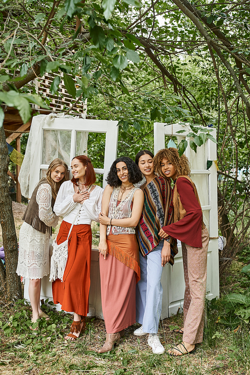 full length of cheerful and multiethnic women in boho outfits standing in modern retreat center