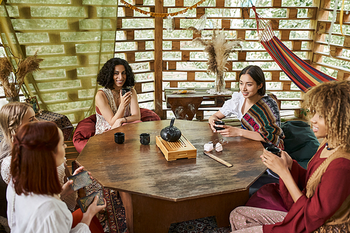 women retreat concept, positive multiethnic girlfriends drinking tea and talking at wooden table