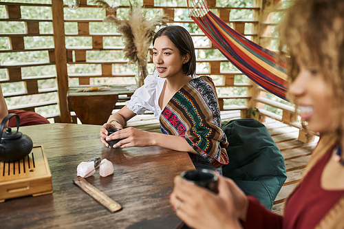 happy young woman in boho style clothes drinking tea at wooden table in retreat center