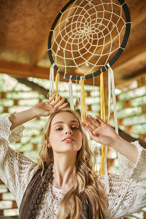 portrait of young boho style woman posing near dream catcher in cottage of retreat center