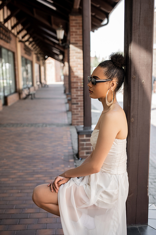 side view of charming african american woman in wedding dress and sunglasses on urban street