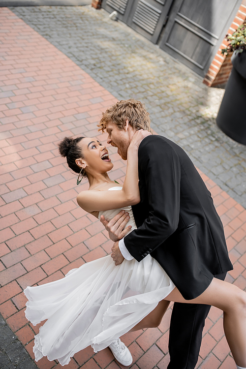 young elegant groom hugging excited african american bride, wedding in european city