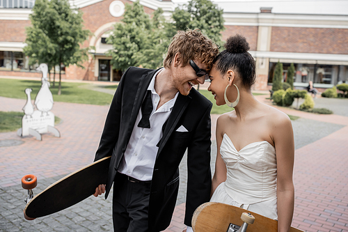 interracial couple with longboard and skateboard having fun on street, wedding attire, sunglasses