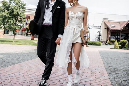 cropped view of elegant multiethnic couple walking with longboard and skateboard, wedding in city