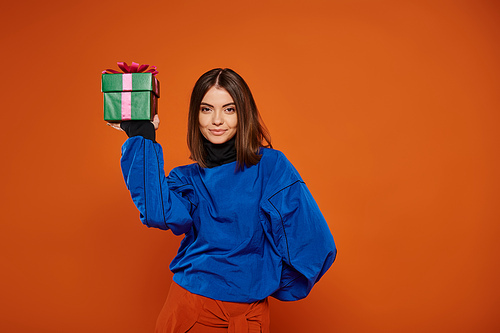 beautiful woman with brunette hair holding wrapped present on orange background, Merry Christmas