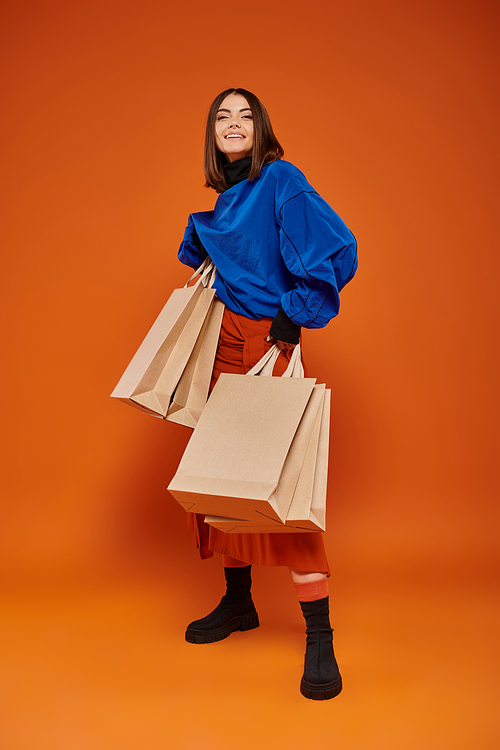 excited woman holding shopping bags and standing on orange backdrop, black friday sales concept