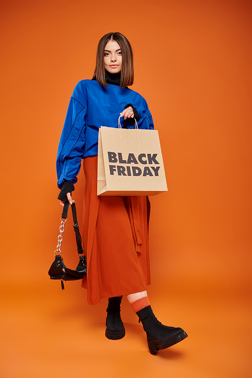 young woman in autumnal clothes standing with trendy handbag and shopping bag on black friday