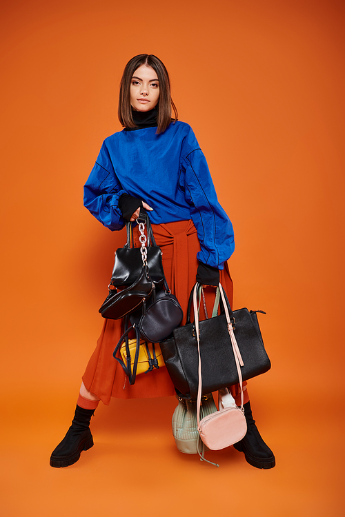 young woman in autumnal clothes holding different bags on orange backdrop, black friday concept