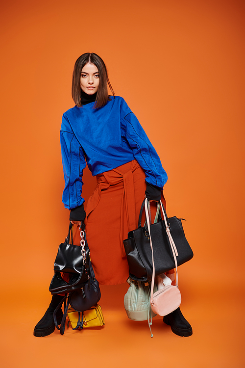 brunette woman in autumnal clothes holding different bags on orange backdrop, black friday concept