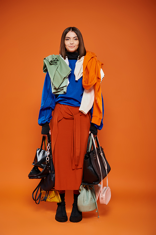 happy woman with warm clothes on shoulders holding handbags on orange backdrop, black friday concept