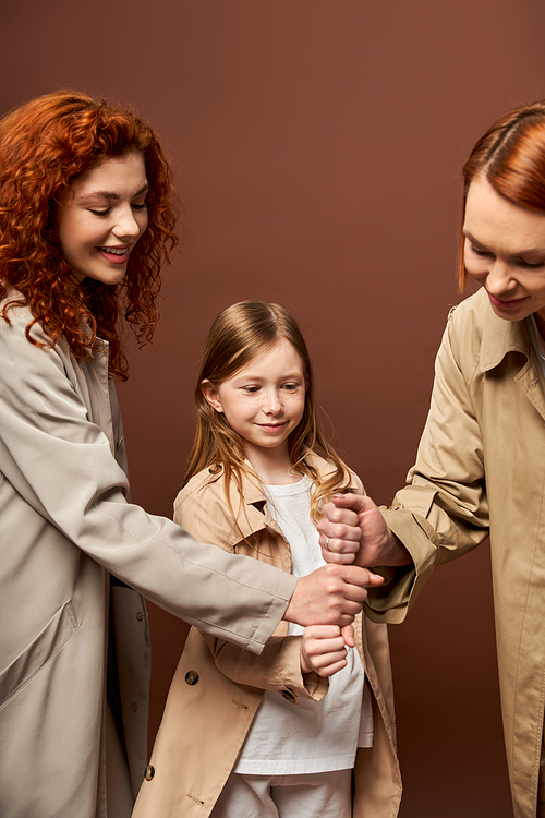 generations, happy family with red hair stacking hands together on brown backdrop, women and girl