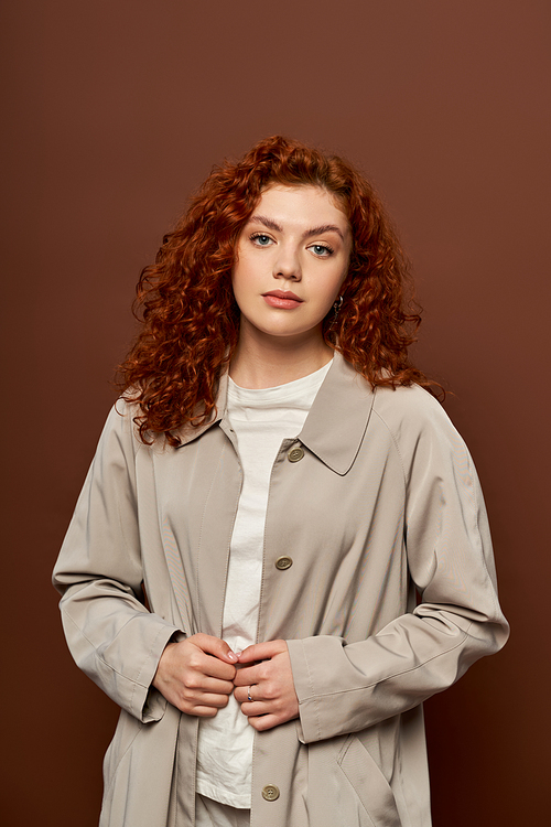 beautiful woman with red curly hair posing in autumn coat on brown background, fall season