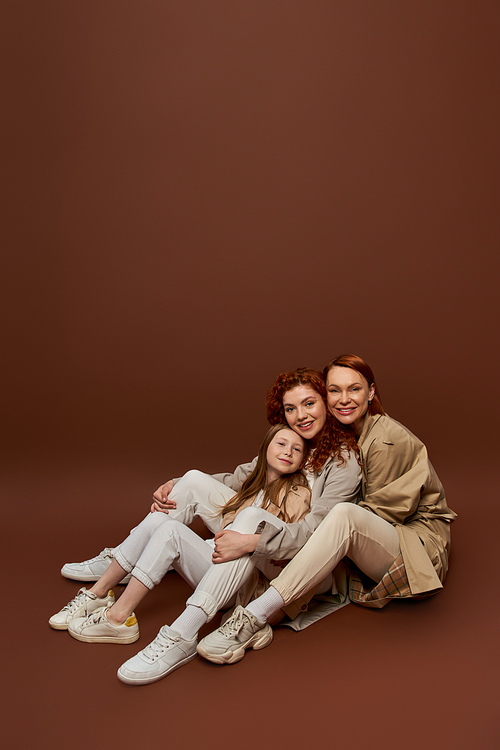 three generations, positive redhead family looking at camera on brown background, women and child