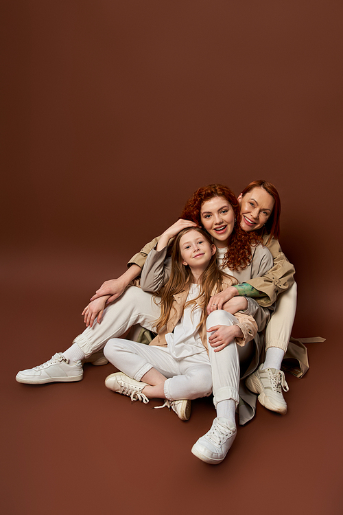 three generations, cheerful redhead family with freckles looking at camera on brown background