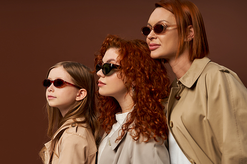 three female generations with red hair posing in sunglasses and coats on brown backdrop, family bond