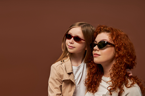 two generations, happy redhead mother and daughter in sunglasses looking away on brown backdrop