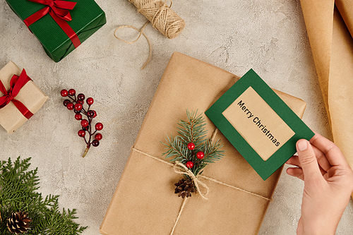 gift box with Merry Christmas greeting card near presents and seasonal decor on textured surface