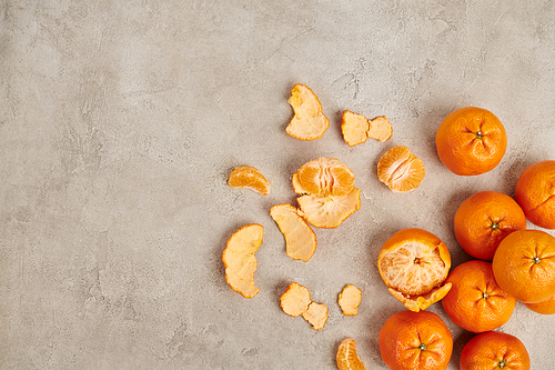 top view of whole and peeled ripe mandarins on grey textured backdrop, Christmas concept