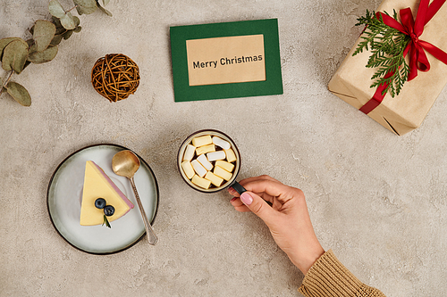 woman with mug of hot chocolate with marshmallows near pudding and Merry Christmas greeting card